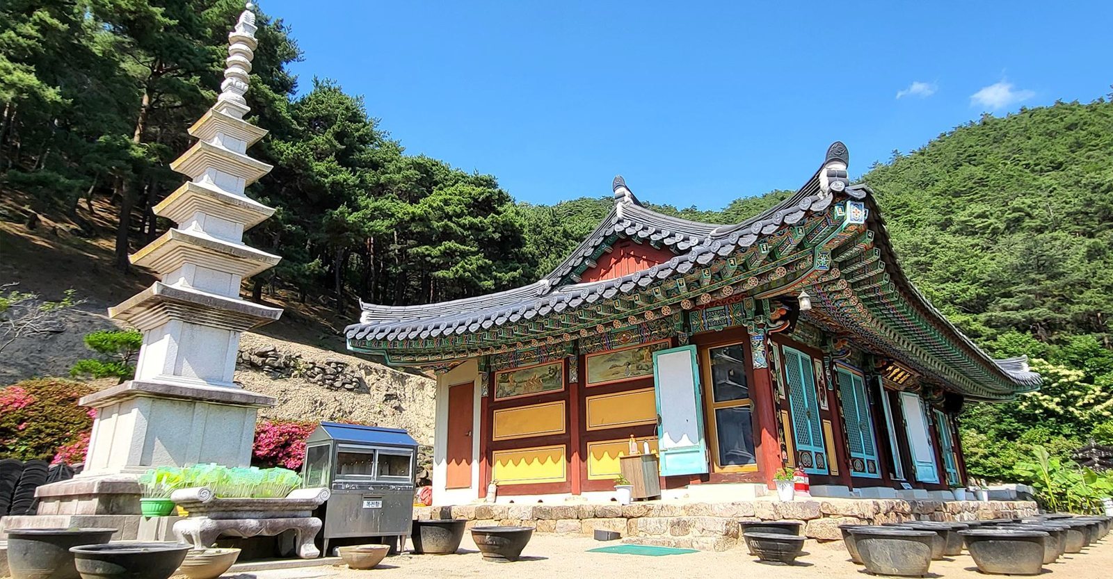 맑은 하늘 아래 단청을 입힌 대웅전 일대와 흰 석탑, 마당에 놓인 옹기들